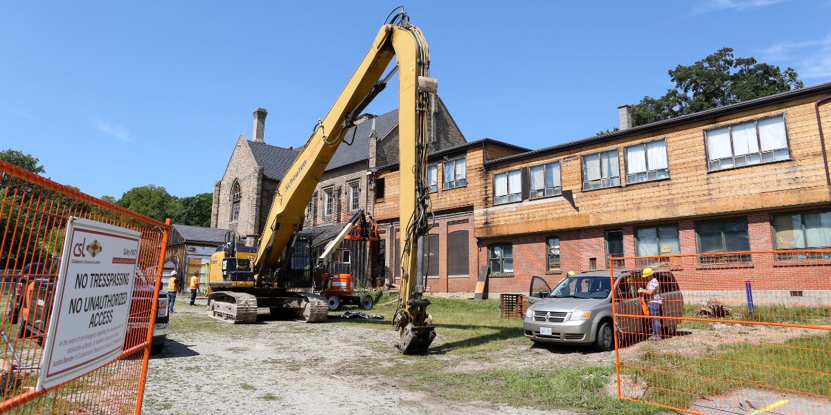 Exterior image of the side and back of the Bawcutt Centre. Construction crews are onsite and removing a portion of an outbuilding. A large digger is parked in the foreground.