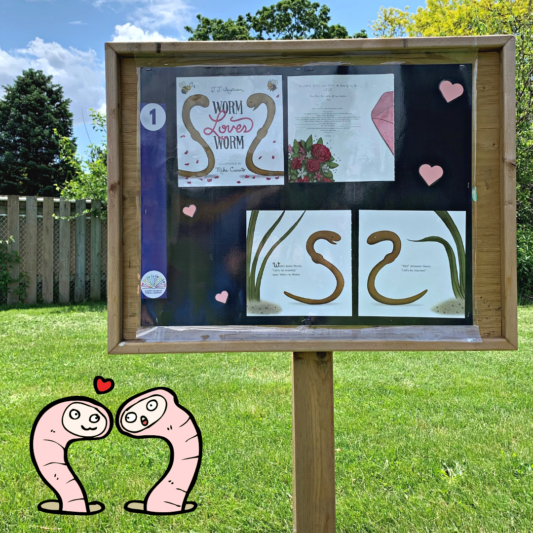 Storybook Walk sign featuring the cover and first page of the book "Worm Loves Worm" by J. J. Austrian. The sign is posted in a parklike setting. There is a small cartoon graphic of two worms and a little heart located in the bottom left of the graphic.