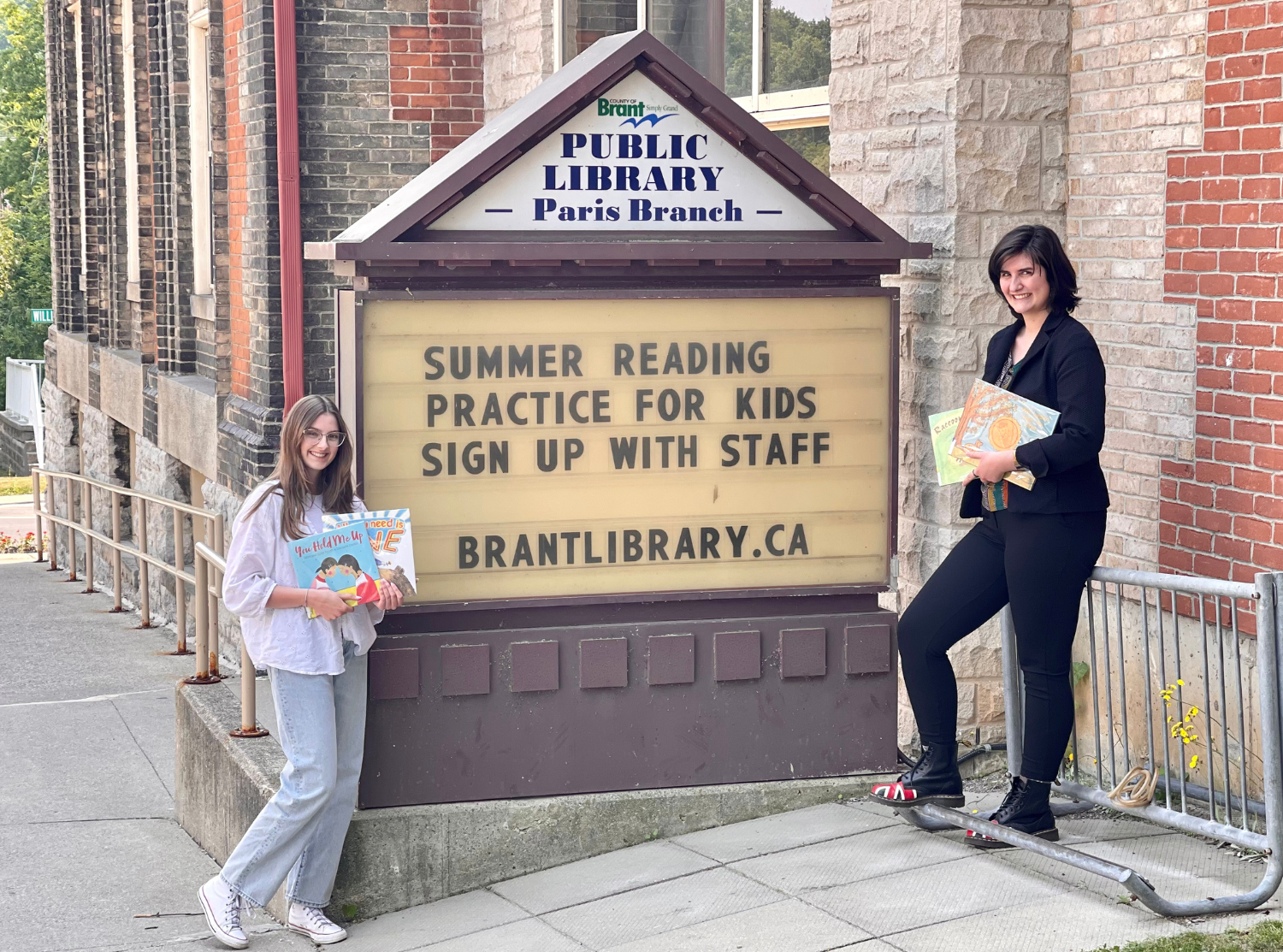 Two Read It tutors standing on either side of a library's outdoor sign.