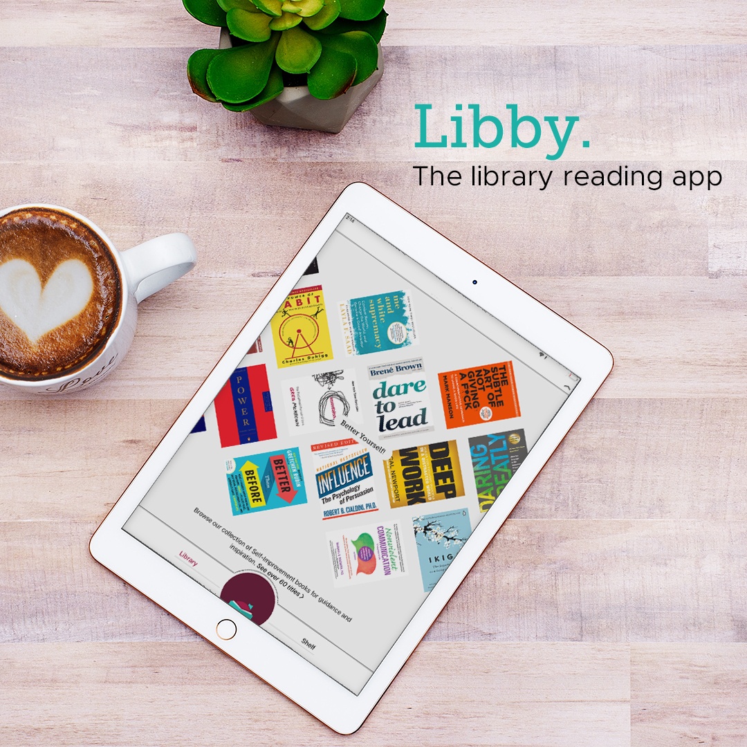 Tablet device lying on wooden table next to plant and cup of coffee. The screen highlights eBook covers found in the Libby Collection.