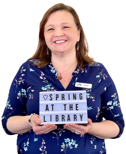 Cheerful woman holding a marquee sign that reads, "Spring at the Library."